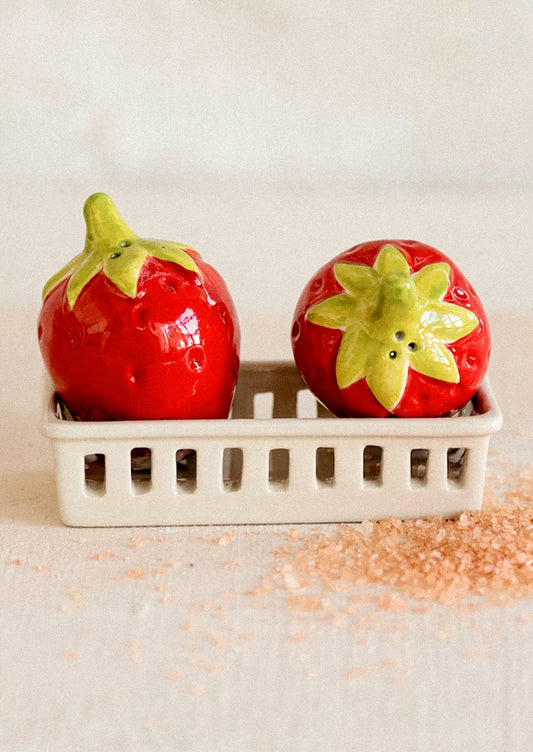 A salt and pepper shaker set depicting red strawberries in a white berry basket.
