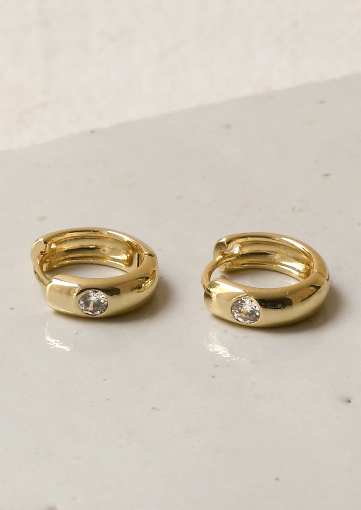 A pair of gold hoop earrings with a round diamond on the front.