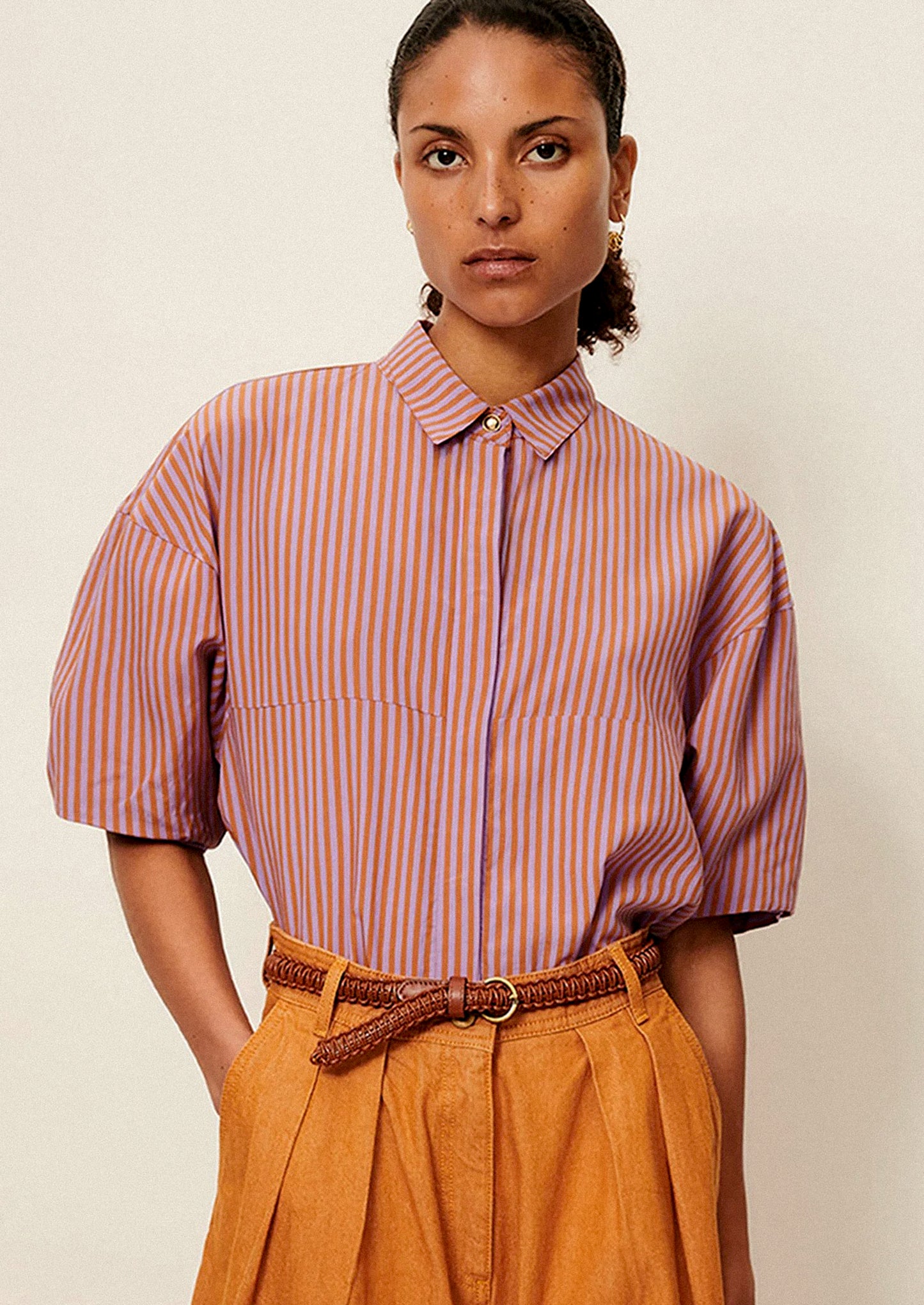 A woman wearing a short collared shirt in orange and purple stripes.