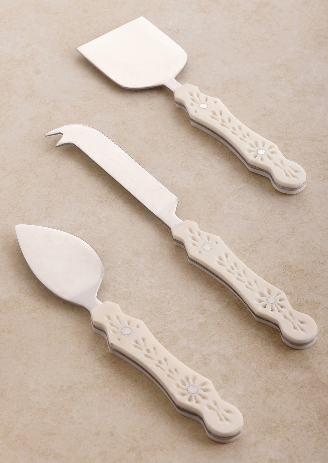 Three different cheese knife styles in silver with eyelet detailed cream resin handles.