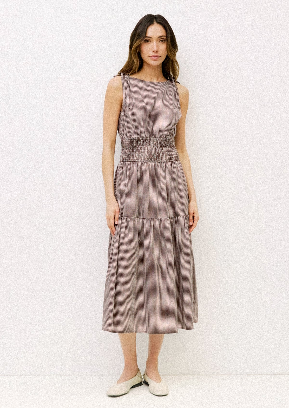 Woman wearing a sleeveless, tiered dress against a white background