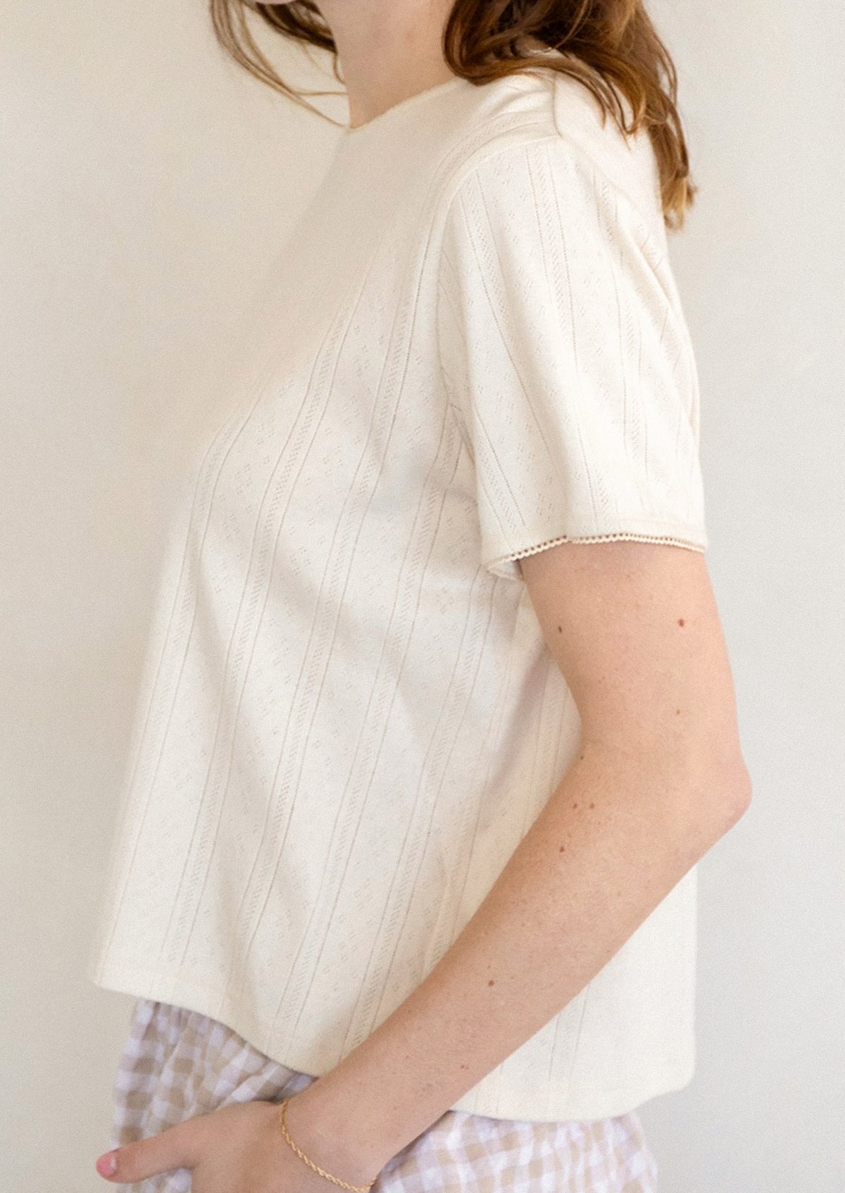 A woman wearing a pointelle stitch tee in cream.