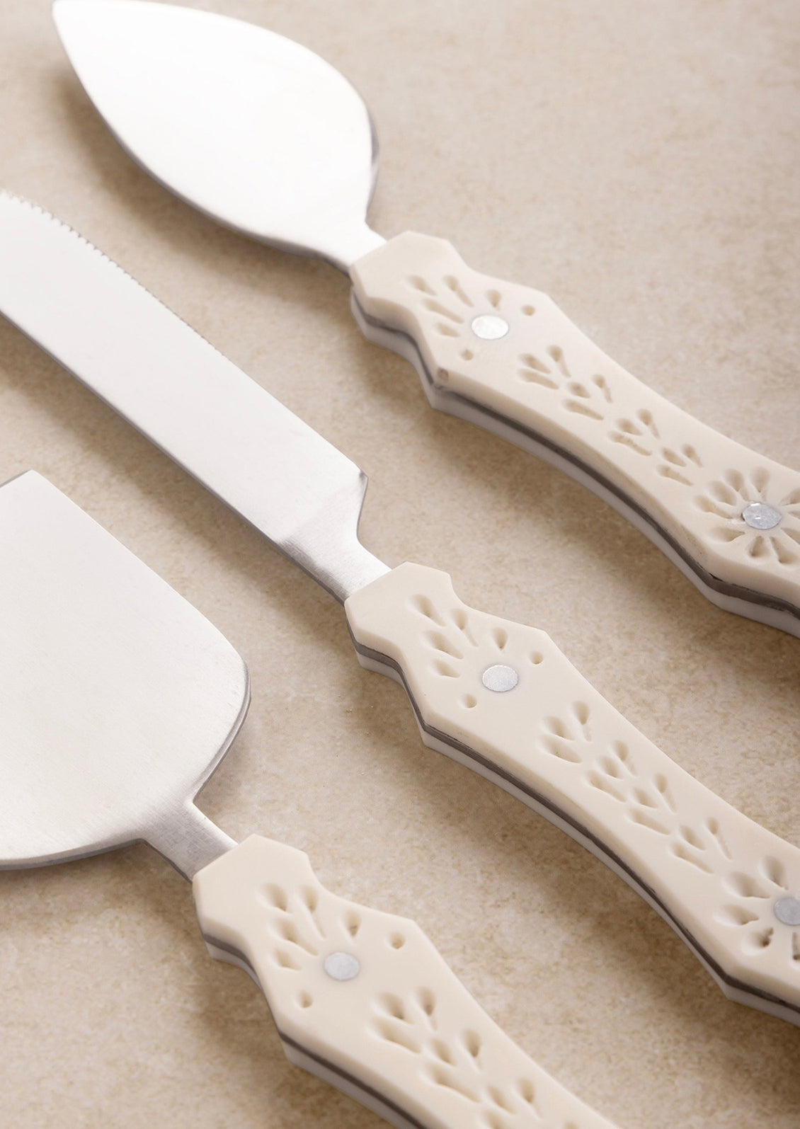 Three different cheese knife styles in silver with eyelet detailed cream resin handles.