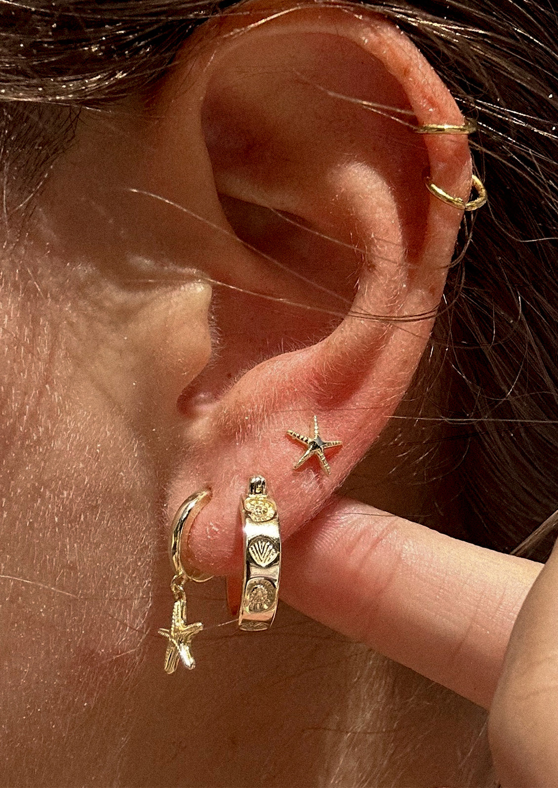 Close-up of an ear with gold hoop earrings and a star-shaped earring.