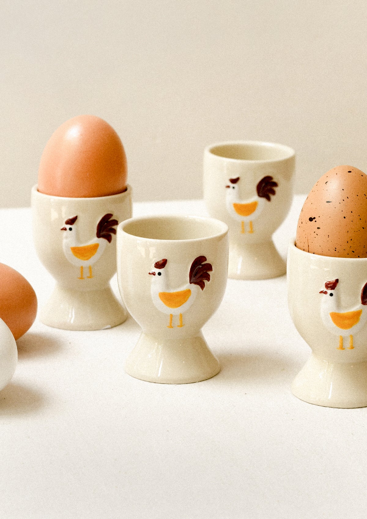 Set of four ceramic egg cups with chicken designs on a white surface.