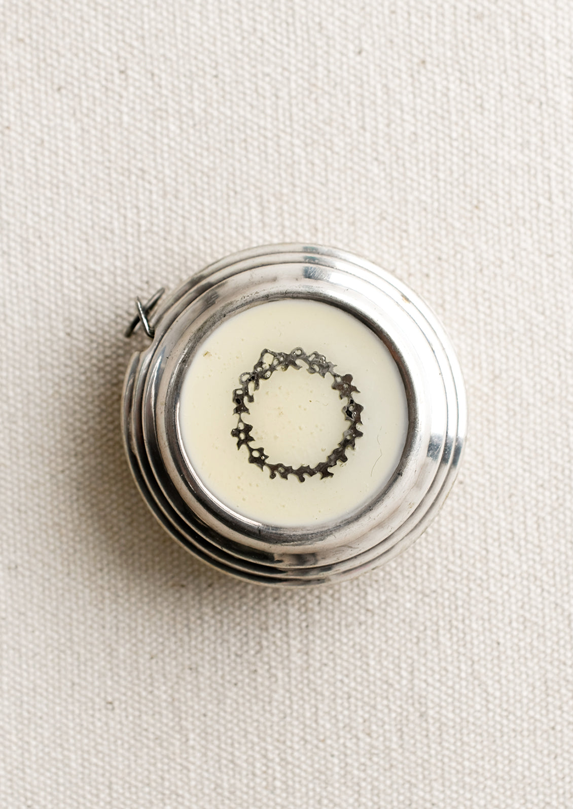 A round silver-tone measuring tape with cream enamel and wreath design.