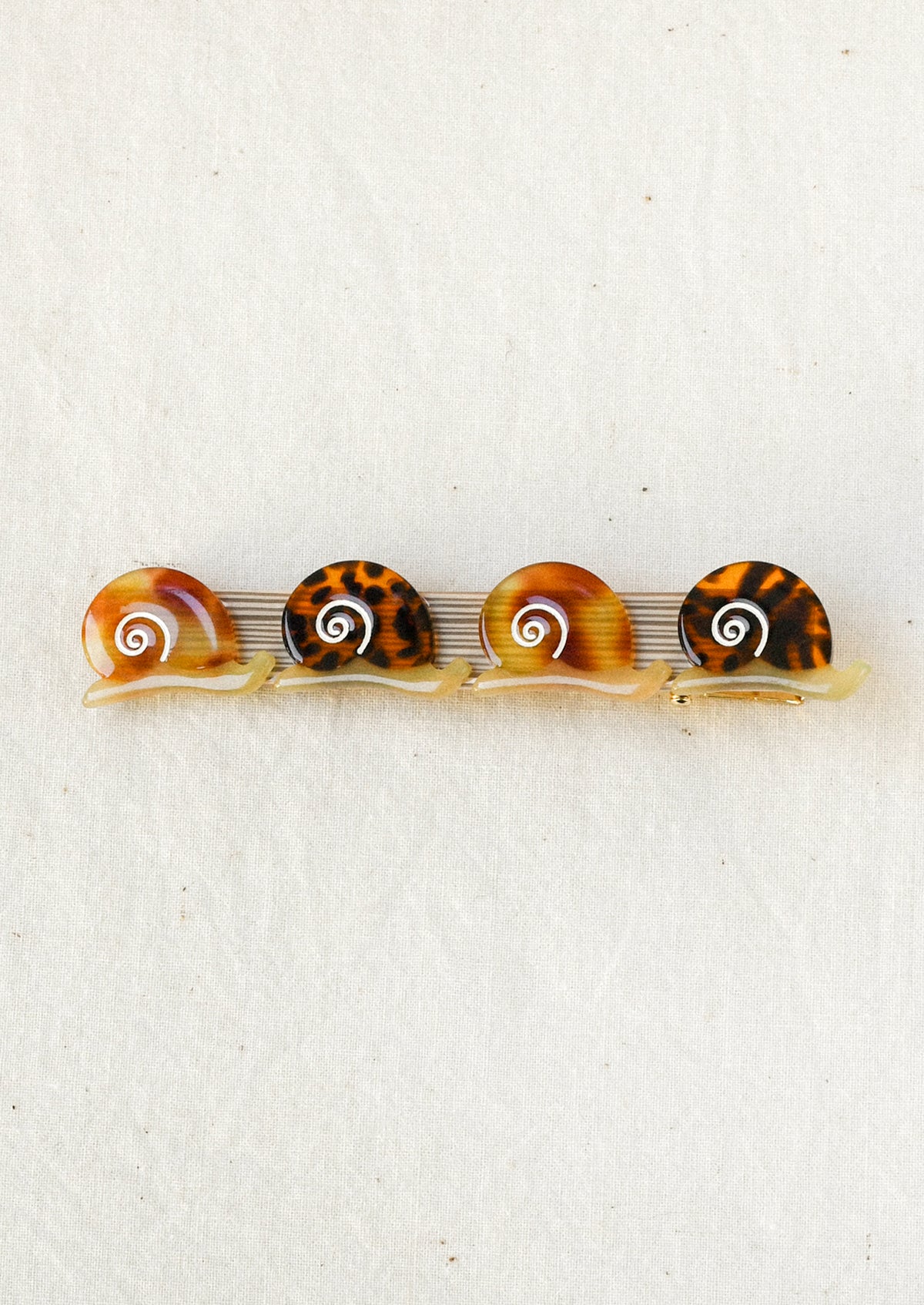 A gold hair barrette decorated with small brown snails with tortoise shell and gradient brown shell patterns.