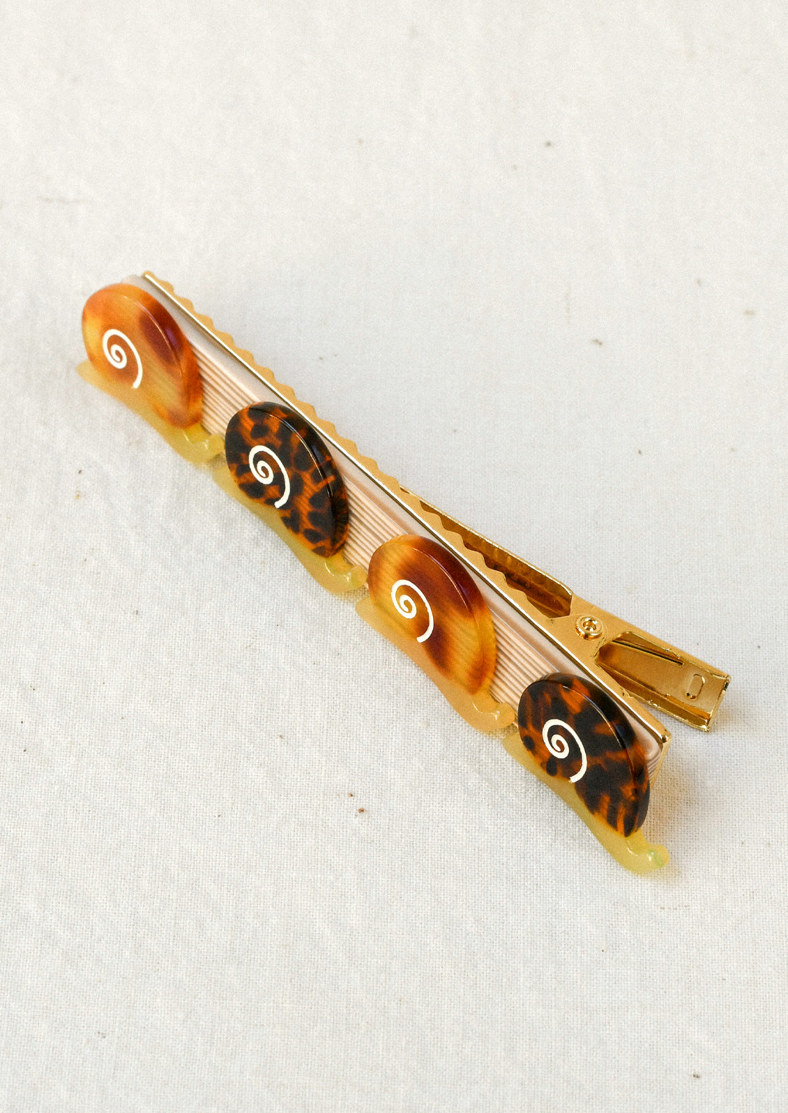 A gold hair barrette decorated with small brown snails with tortoise shell and gradient brown shell patterns.