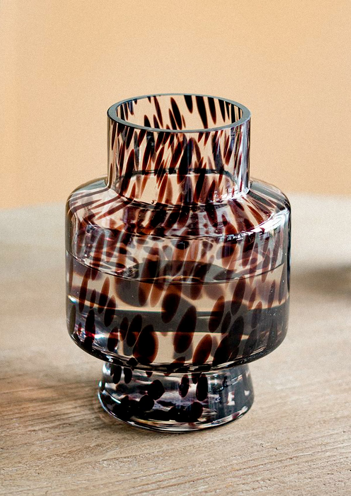 A small clear glass vase with a dark brown and black abstract spotted pattern.