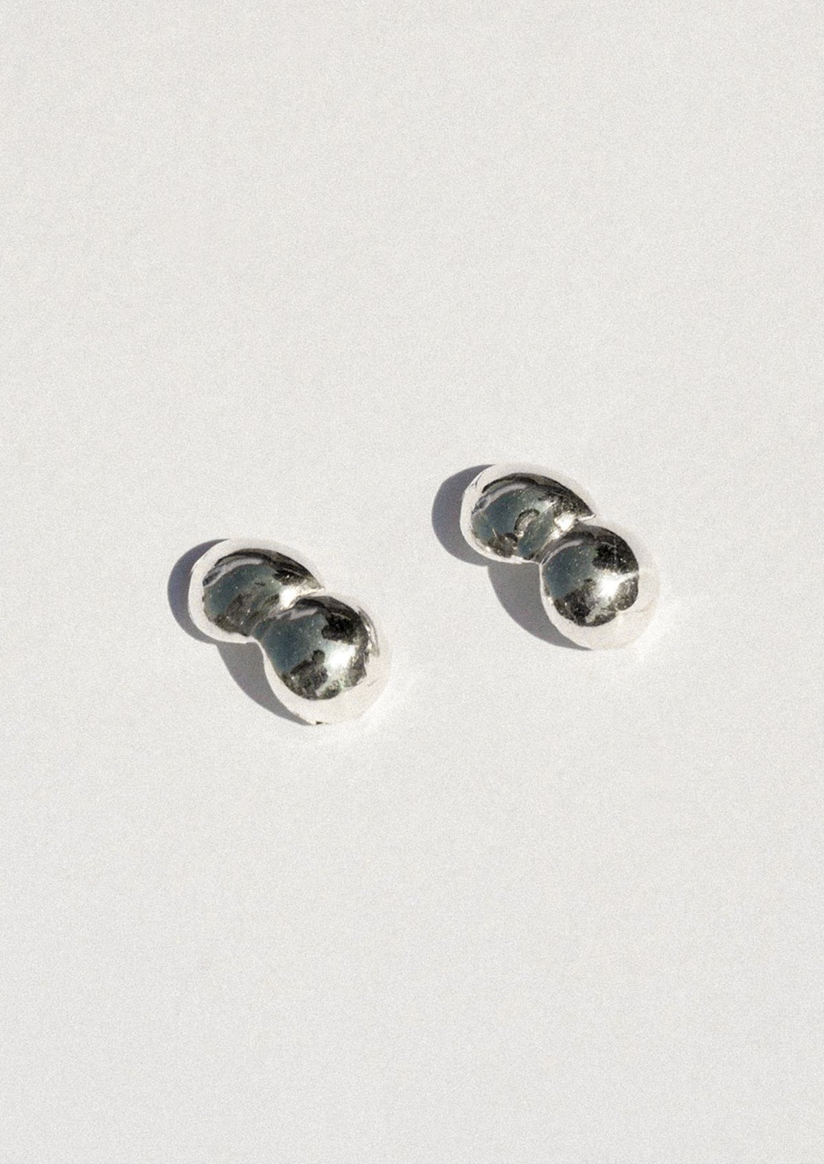 A pair of small silver stud earrings with a double-bubble design, photographed on a clean white background with soft shadows.