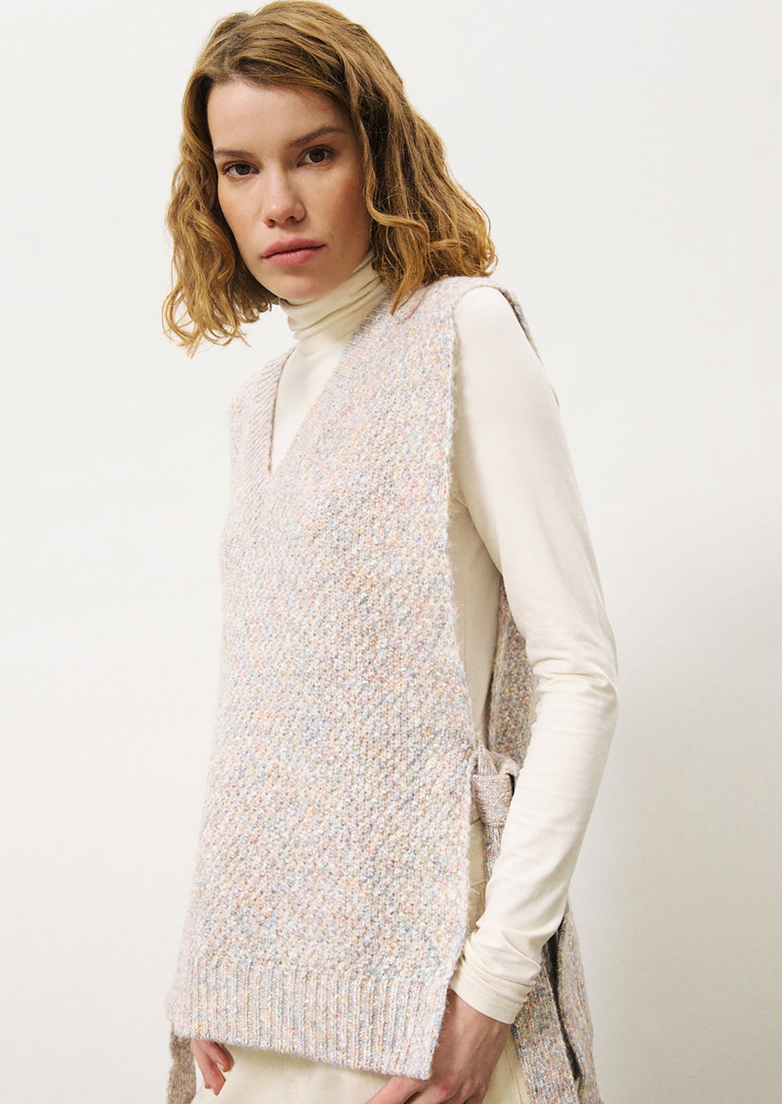 A woman wearing a long tunic style sweater vest in pastel yarn.
