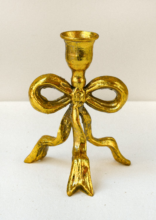 A metal taper holder in the shape of a bow with a gold finish.