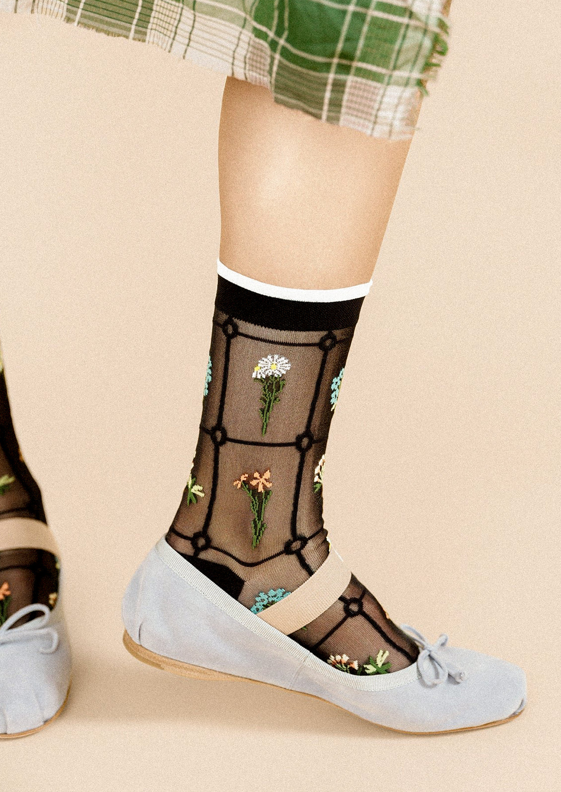 A person wearing a pair of semi-sheer black socks with various embroidered flowers.