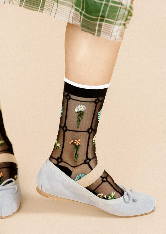 A person wearing a pair of semi-sheer black socks with various embroidered flowers.
