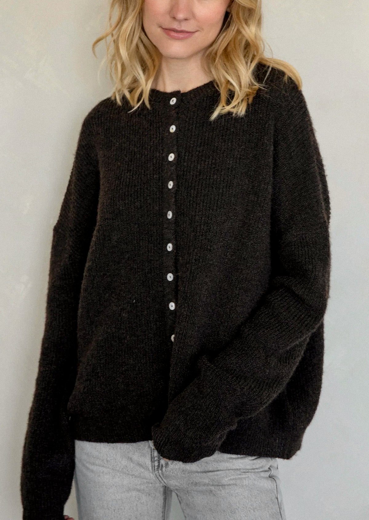 A woman wearing a chocolate brown cardigan with white button front.