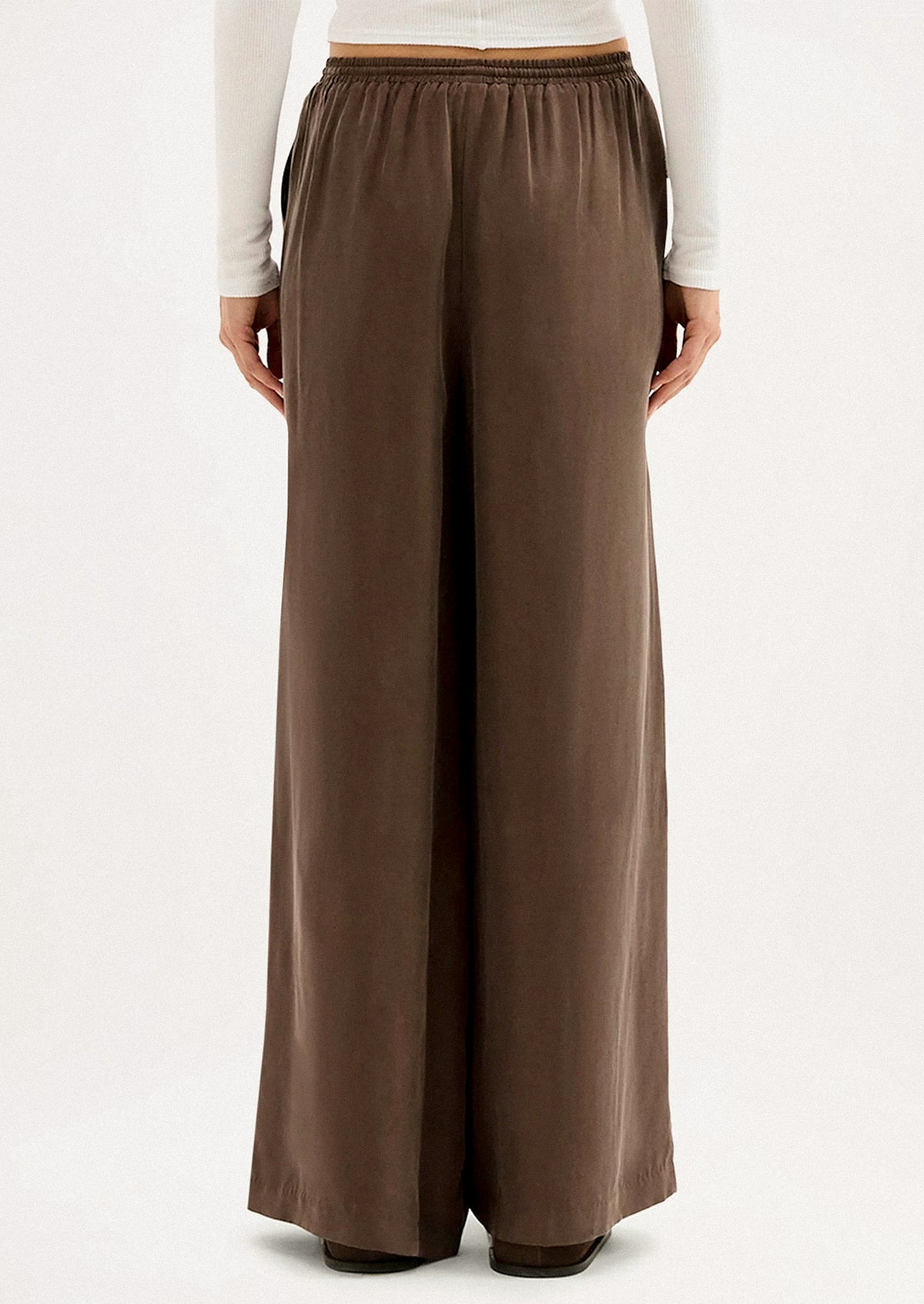 A person wearing a pair of long wide leg pants in brown cupro.