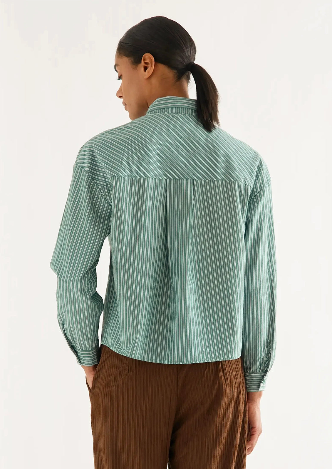 A woman wearing a long sleeve blouse with neck tie detail, in allover green and white stripe.