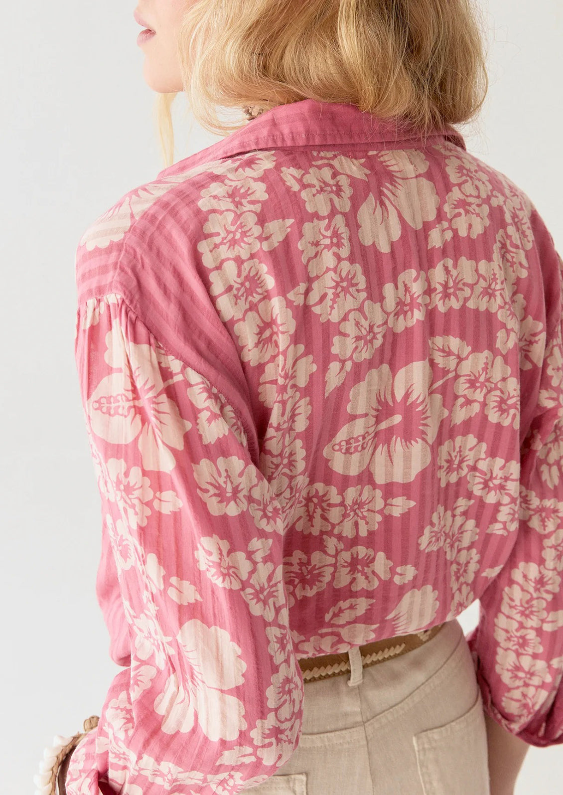 A person wearing a pink cotton shirt with tonal pinstripes and Hawaiian floral pattern.