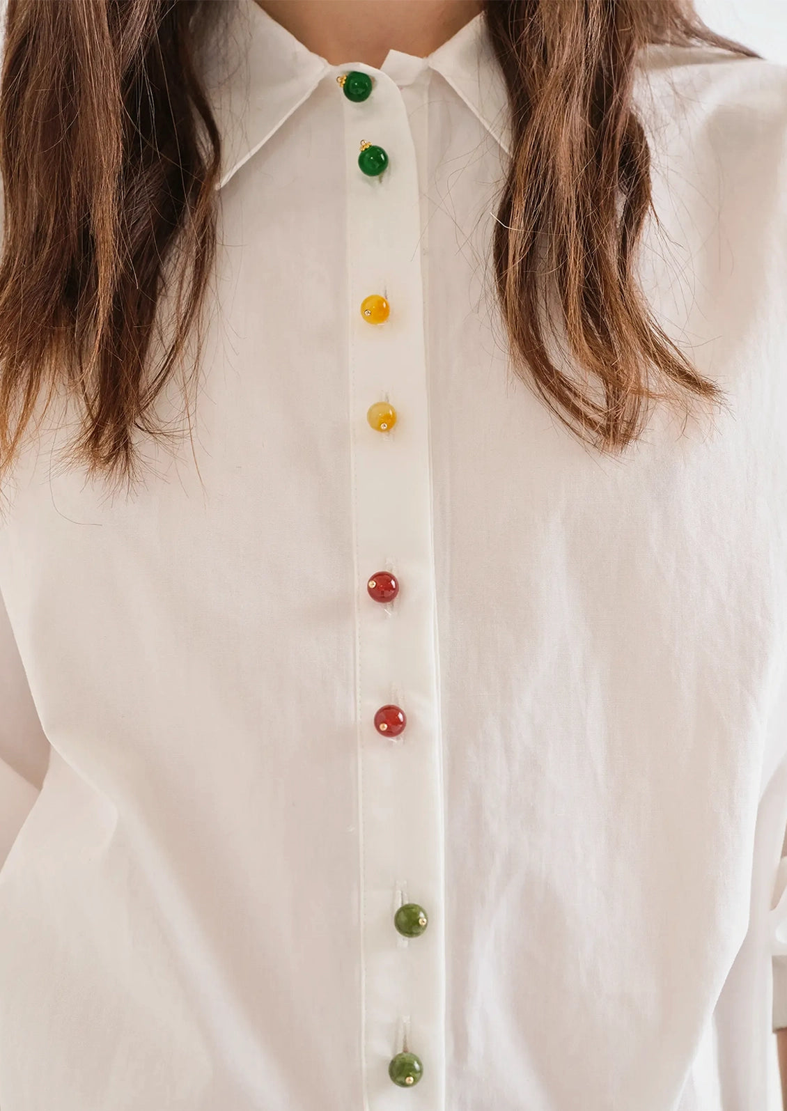 A person wearing a white shirt with multicolor beaded buttons.