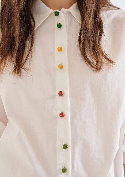 A person wearing a white shirt with multicolor beaded buttons.