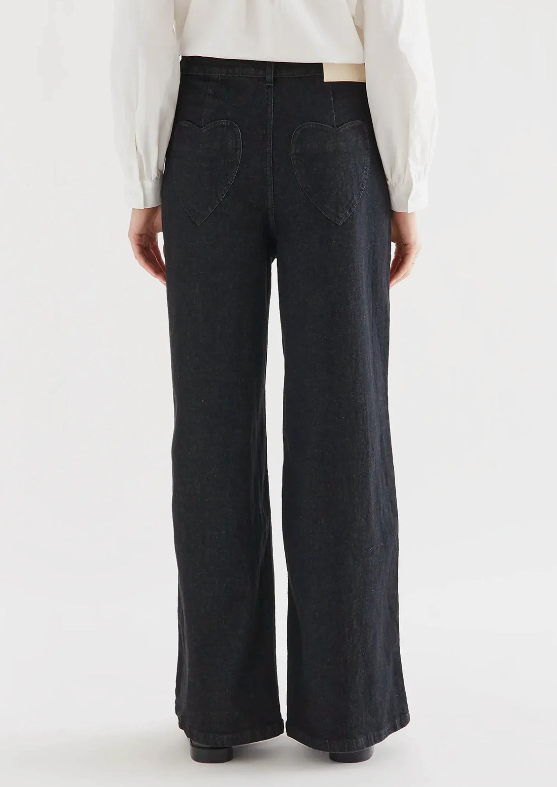A person wearing a pair of black denim jeans with heart shaped rear pockets.