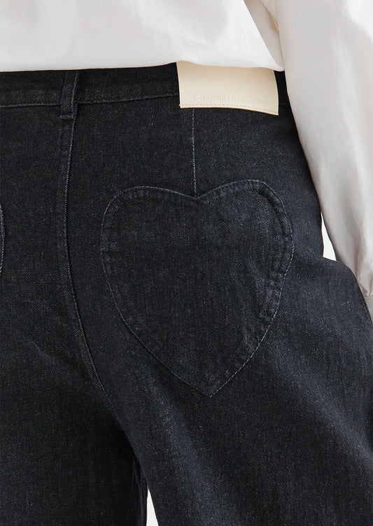 A person wearing a pair of black denim jeans with heart shaped rear pockets.