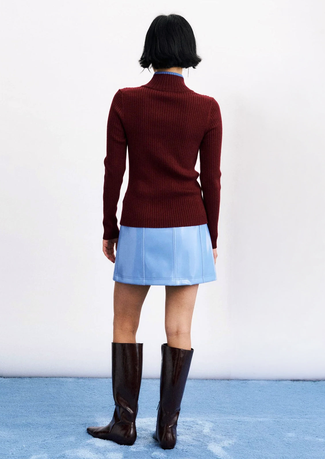 A person wearing a wine red ribbed sweater with mock neck with small blue trim at edge.
