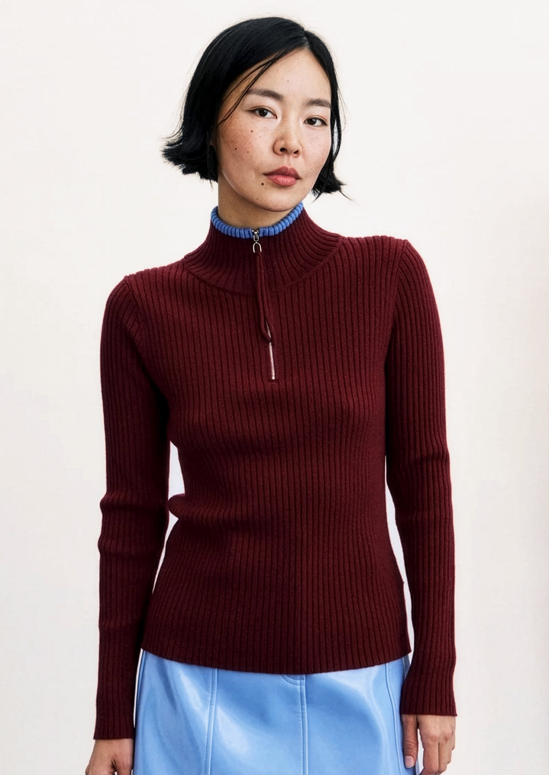 A person wearing a wine red ribbed sweater with mock neck with small blue trim at edge.