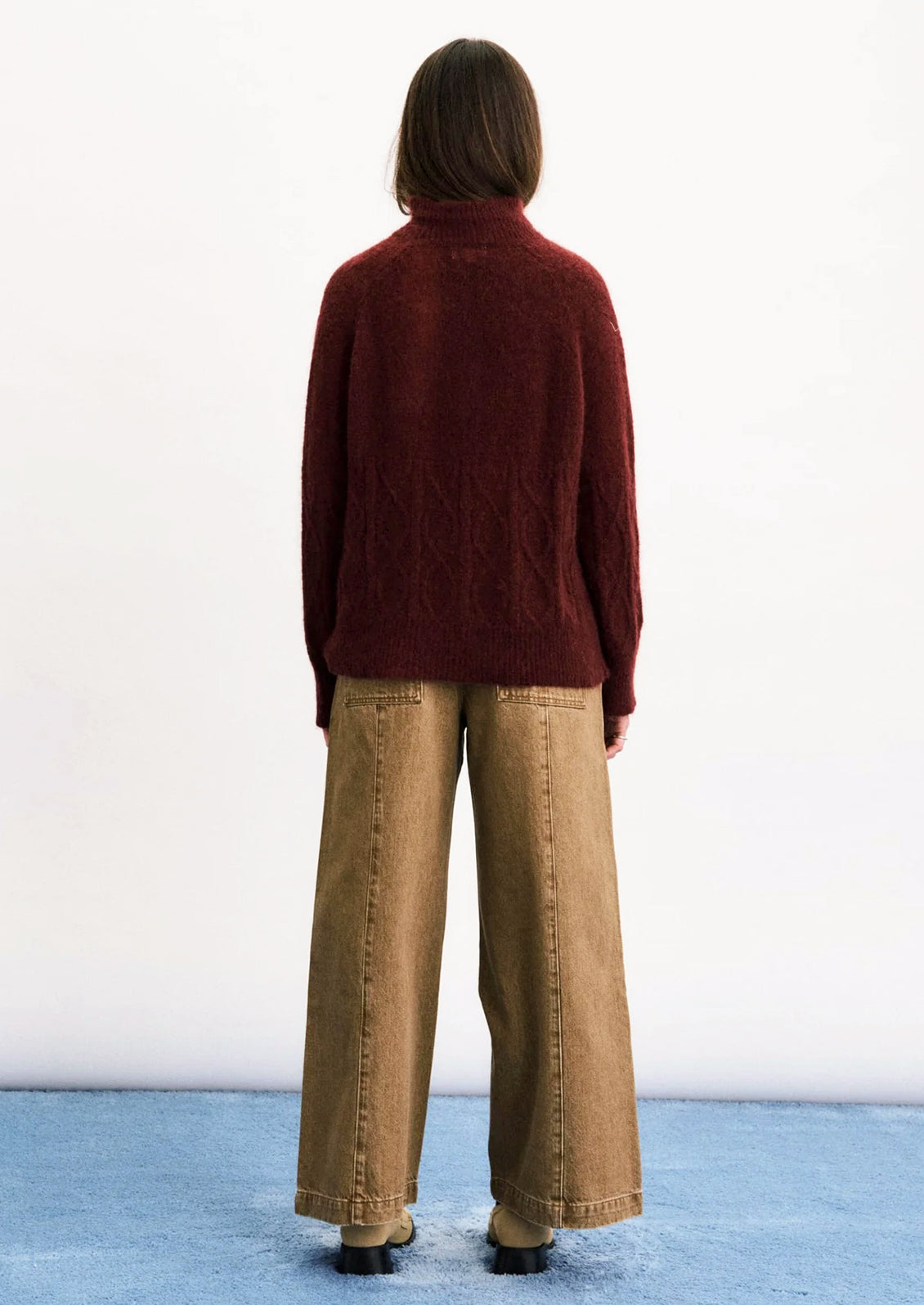 A person wearing a maroon mohair blend sweater with cable stitching detail on lower half.