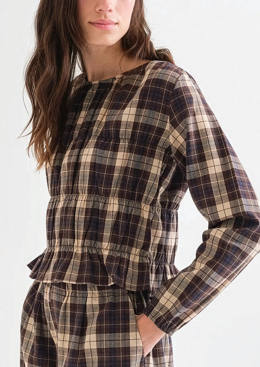A woman wearing a long sleeve plaid top in brown, blue and cream with smocked detailing throughout.