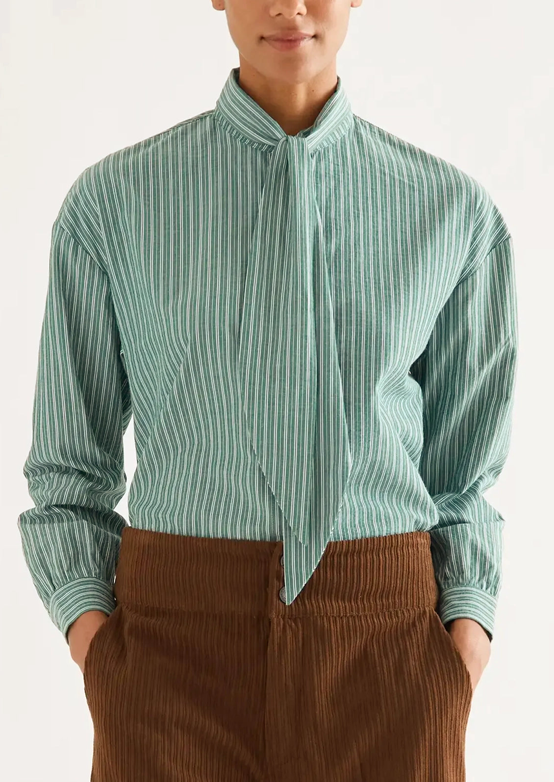 A woman wearing a long sleeve blouse with neck tie detail, in allover green and white stripe.