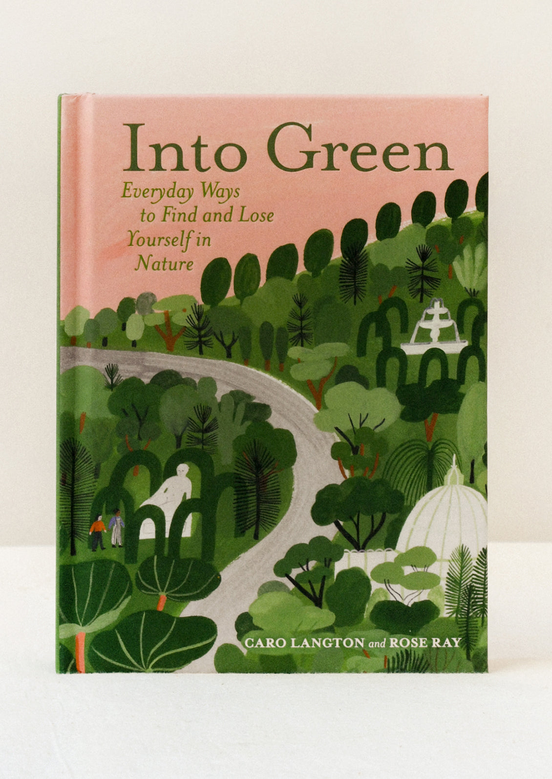 A hardcover copy of the book "Into Green" by Caro Langton and Rose Ray standing on a table. The cover features a green nature scene with a pink sky.
