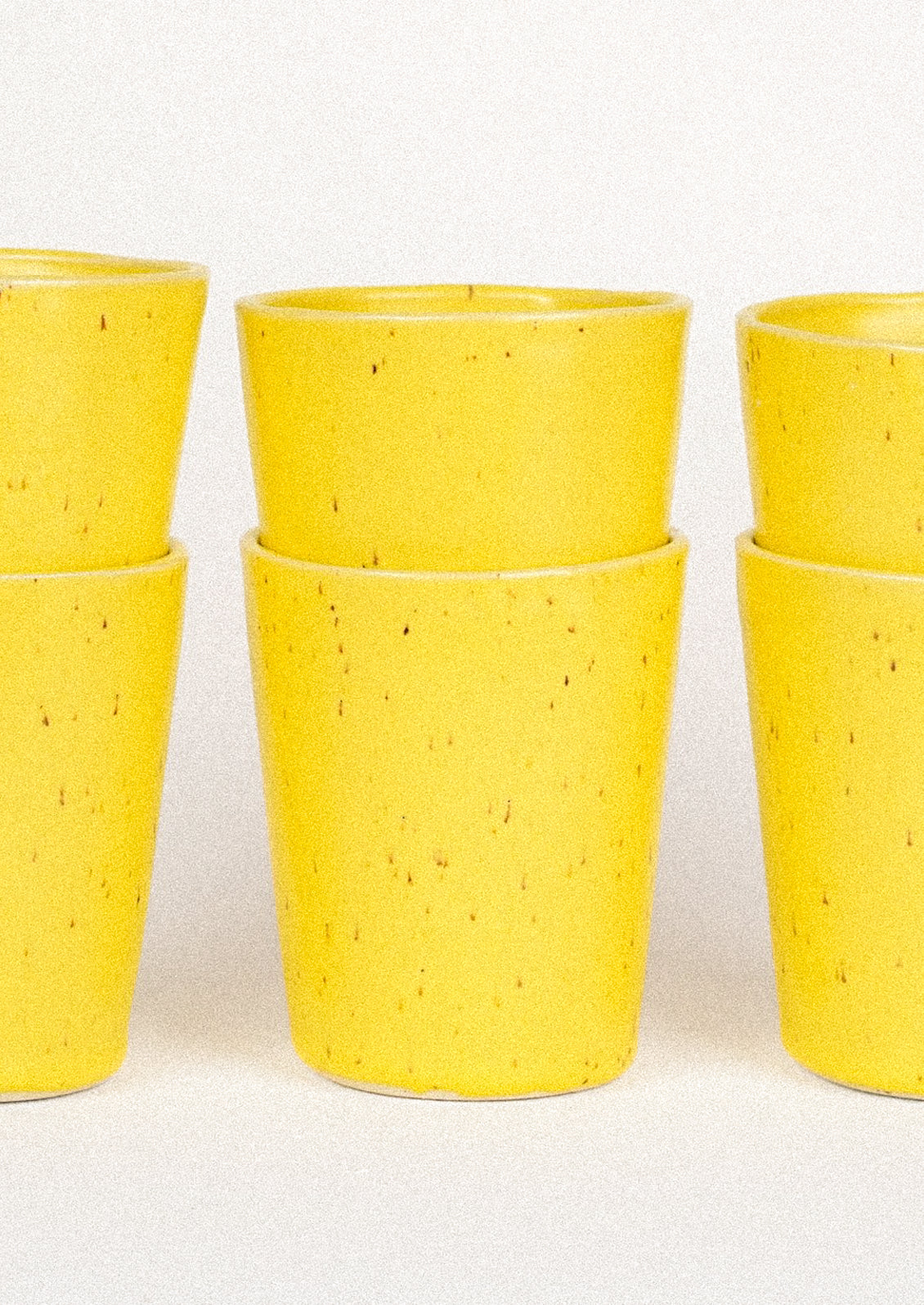 Stacks of 12oz ceramic cups in a speckled yellow color.