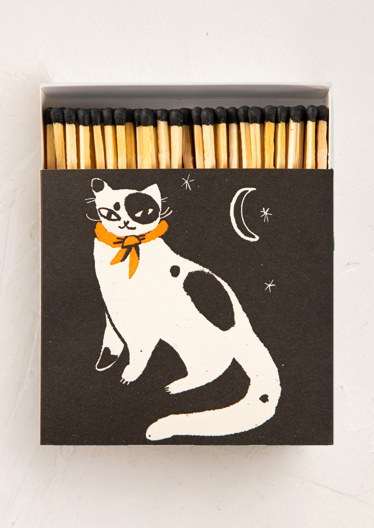 An oversized box of matches. Matches have black tips, and the box is black with a black and white cat illustration, wearing a red neck tie.