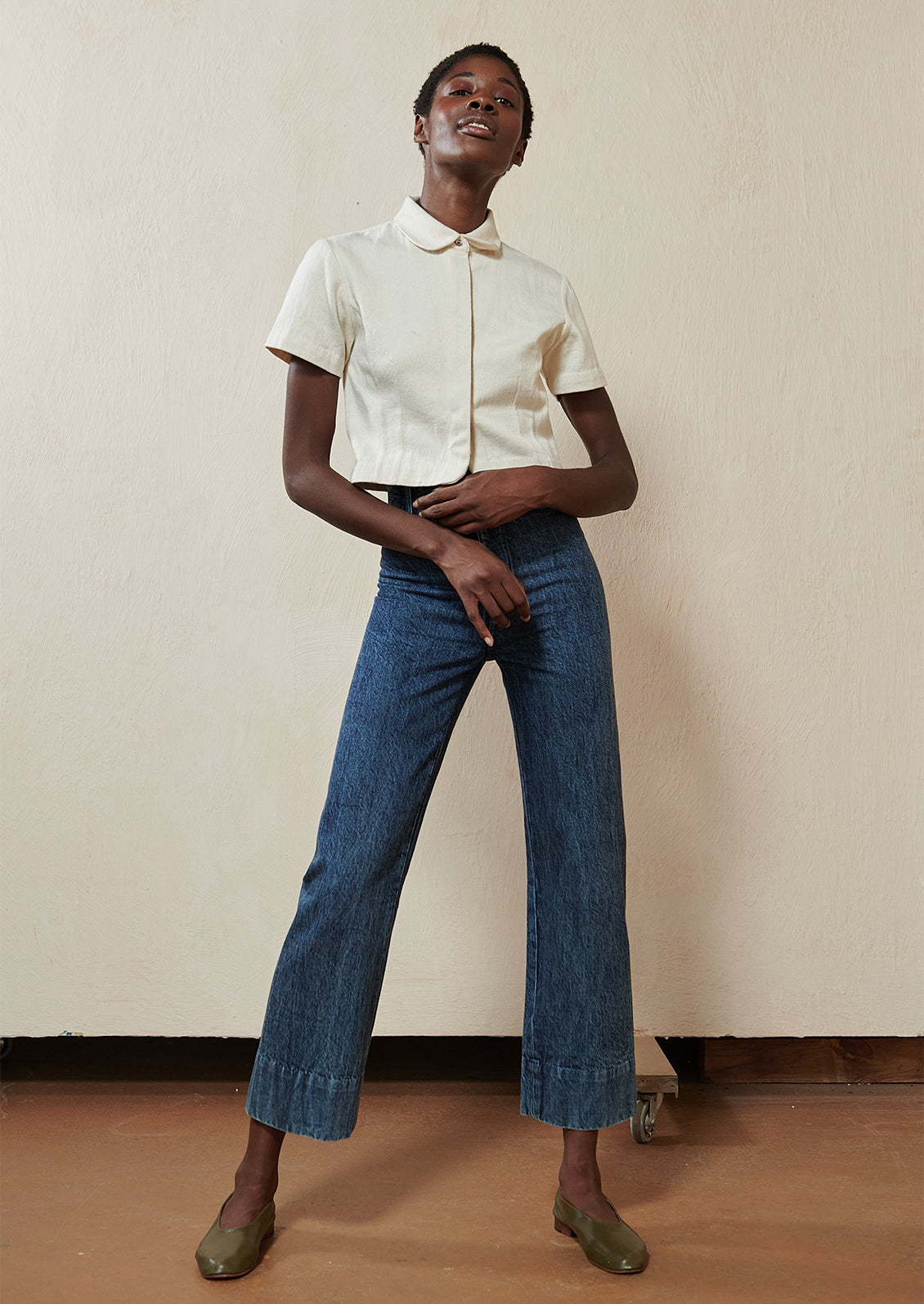 Woman wearing blue jeans, white top, and green flats. 