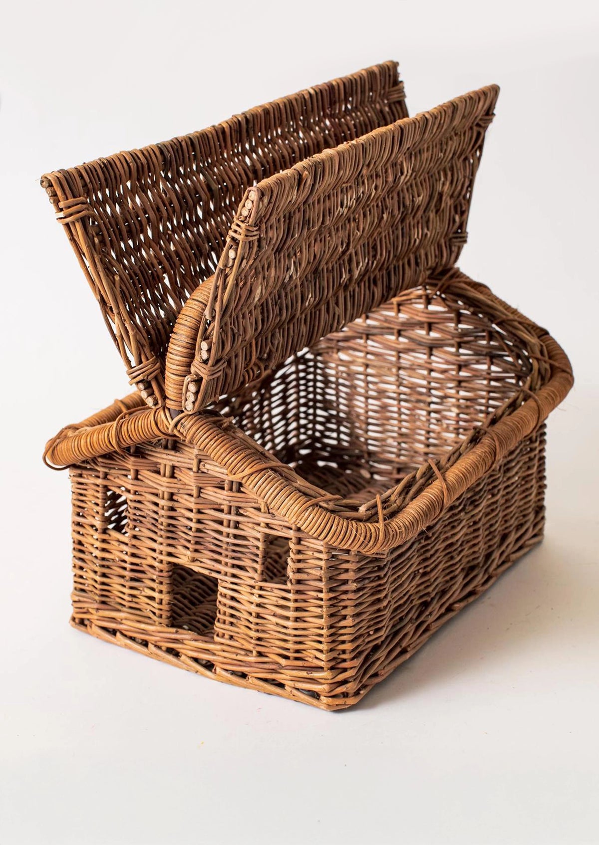 A rustic brown woven wicker basket shaped like a small house, with the lid propped open.