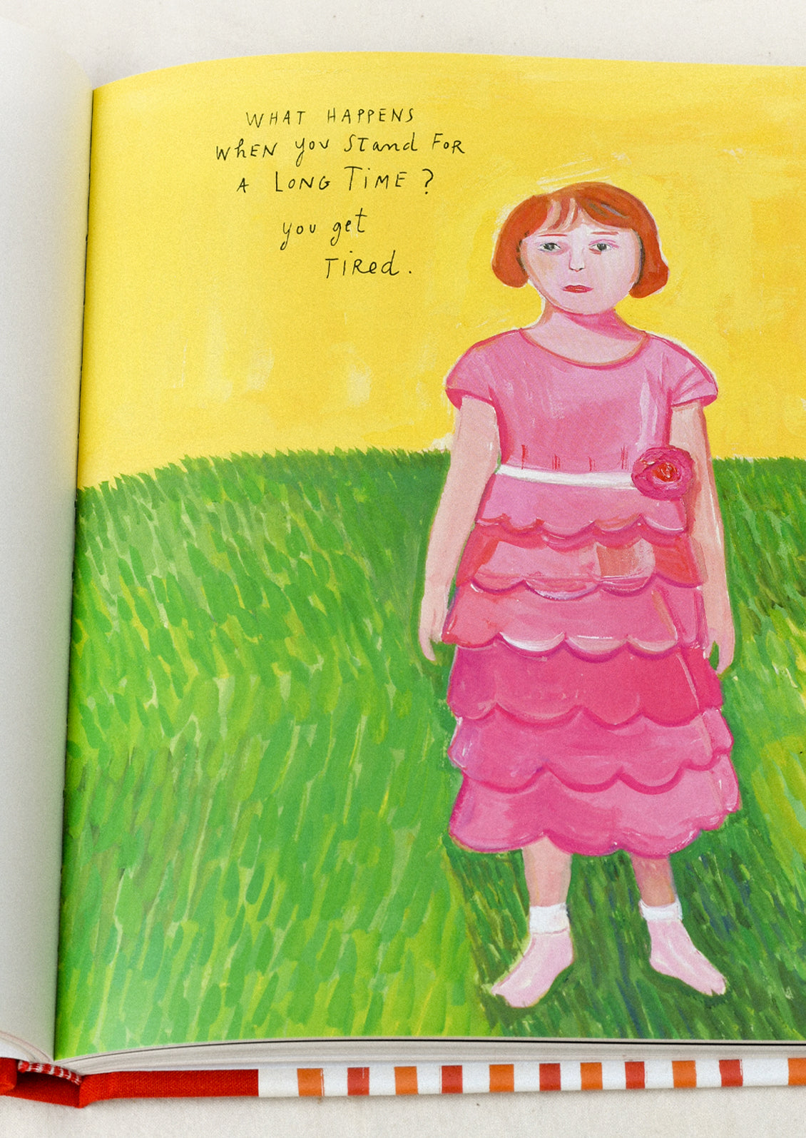 A book titled 'My Favorite Things' by Maira Kalman open on a table showing an illustration of a women in a pink dress standing on a lawn.
