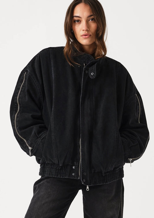 A model wearing a black oversized zip-up jacket with light-colored contrast stitching and black jeans, photographed against a clean white studio background.