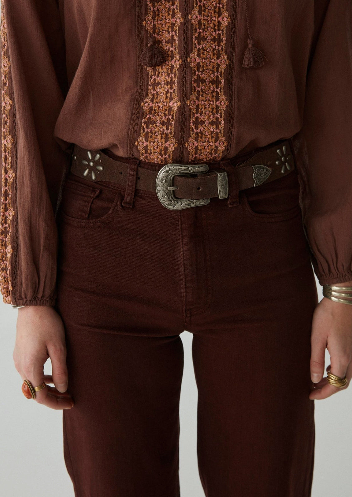 A woman wearing a pair of form fitting, straight leg pants in dark brown.