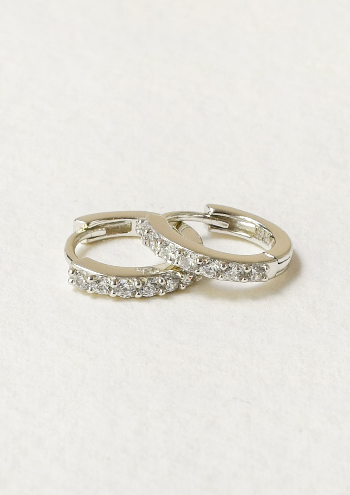 A pair of small huggie hoop earrings with clear pavé-set stones.