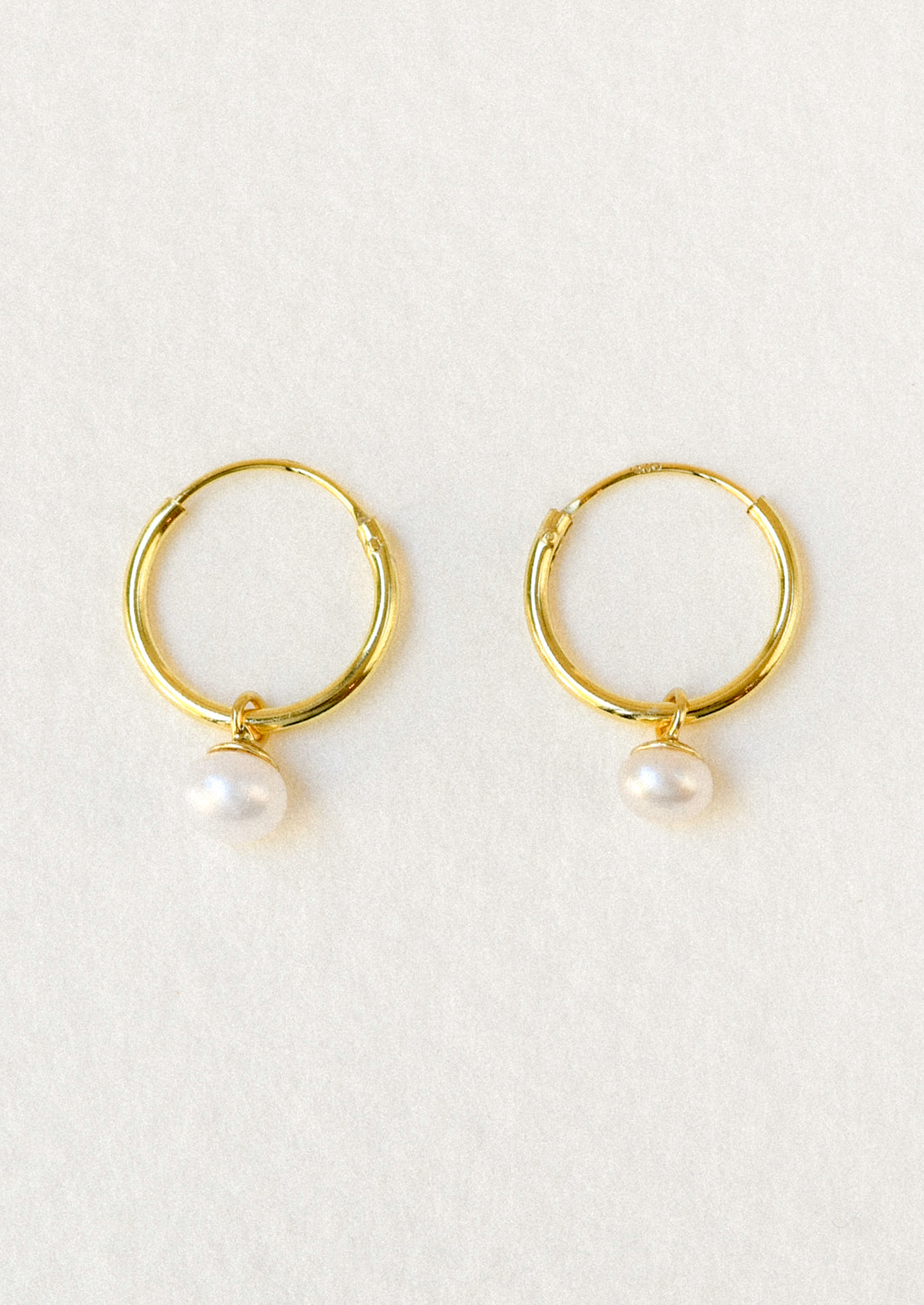 A pair of gold hoop earrings with a dangling freshwater pearl charm.
