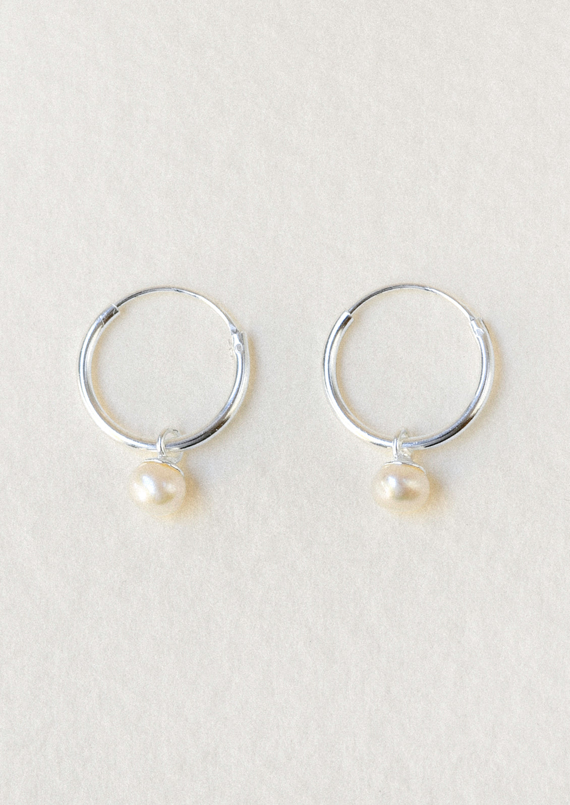 A pair of sterling silver hoop earrings with a dangling freshwater pearl charm.