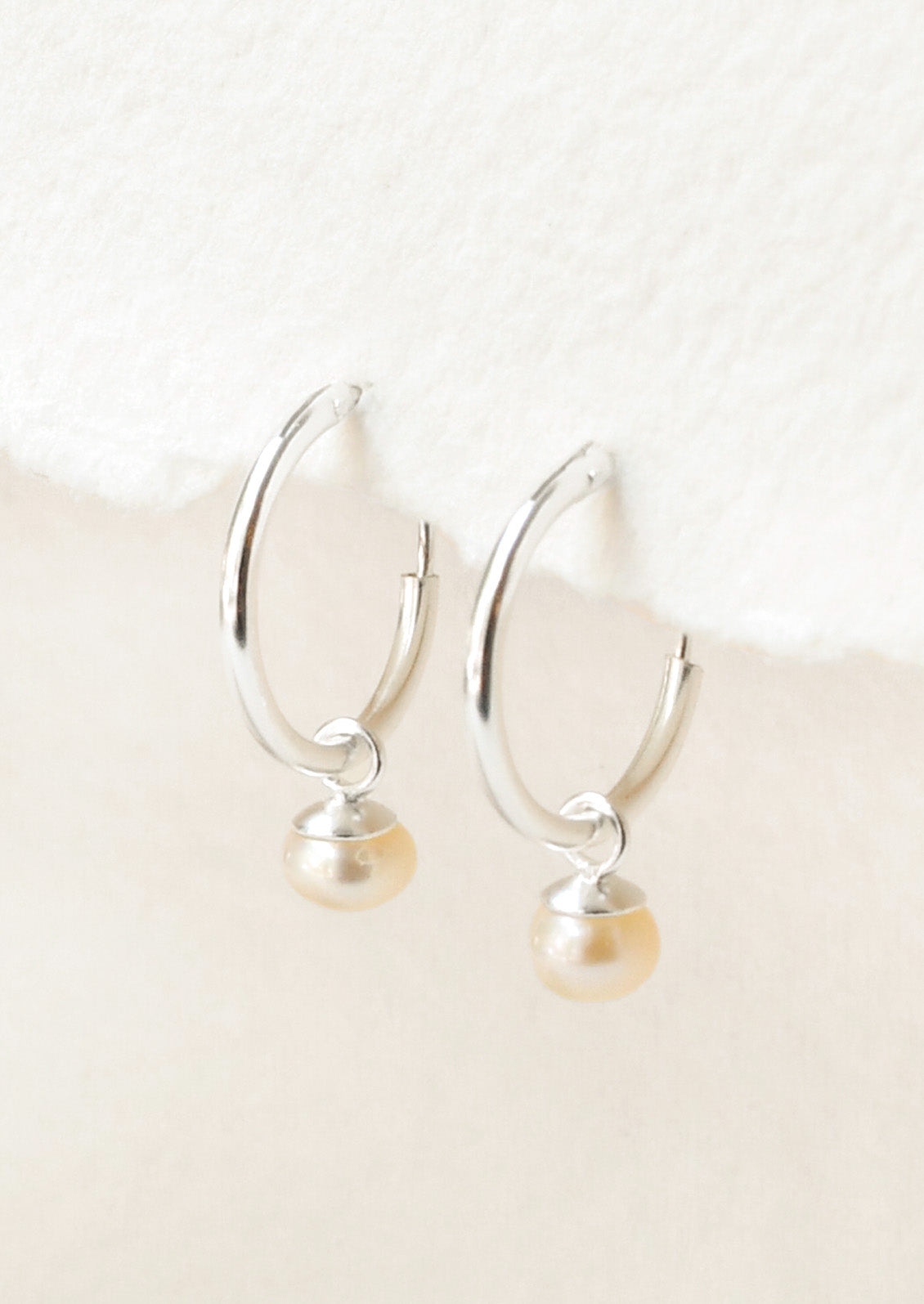 A pair of sterling silver hoop earrings with a dangling freshwater pearl charm.
