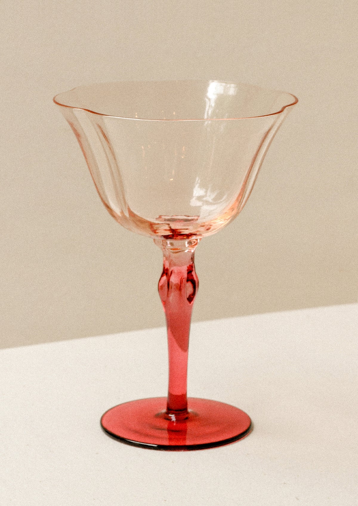 A tall coupe glass with peach top and fuchsia stem.