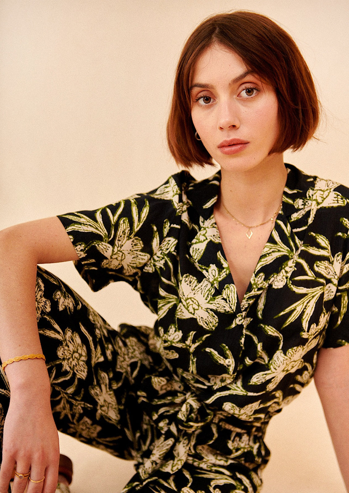 A woman wearing a v-neck collared shirt in black with green and cream floral print.