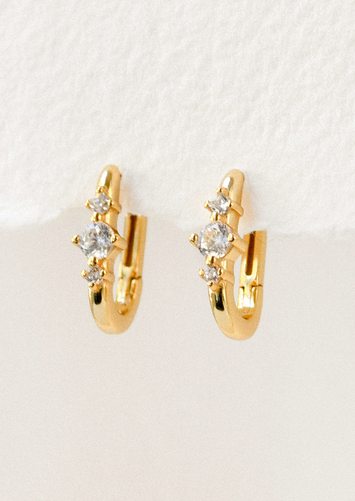 A pair of gold huggie hoop earrings with a trio of pronged cubic zironia gems.