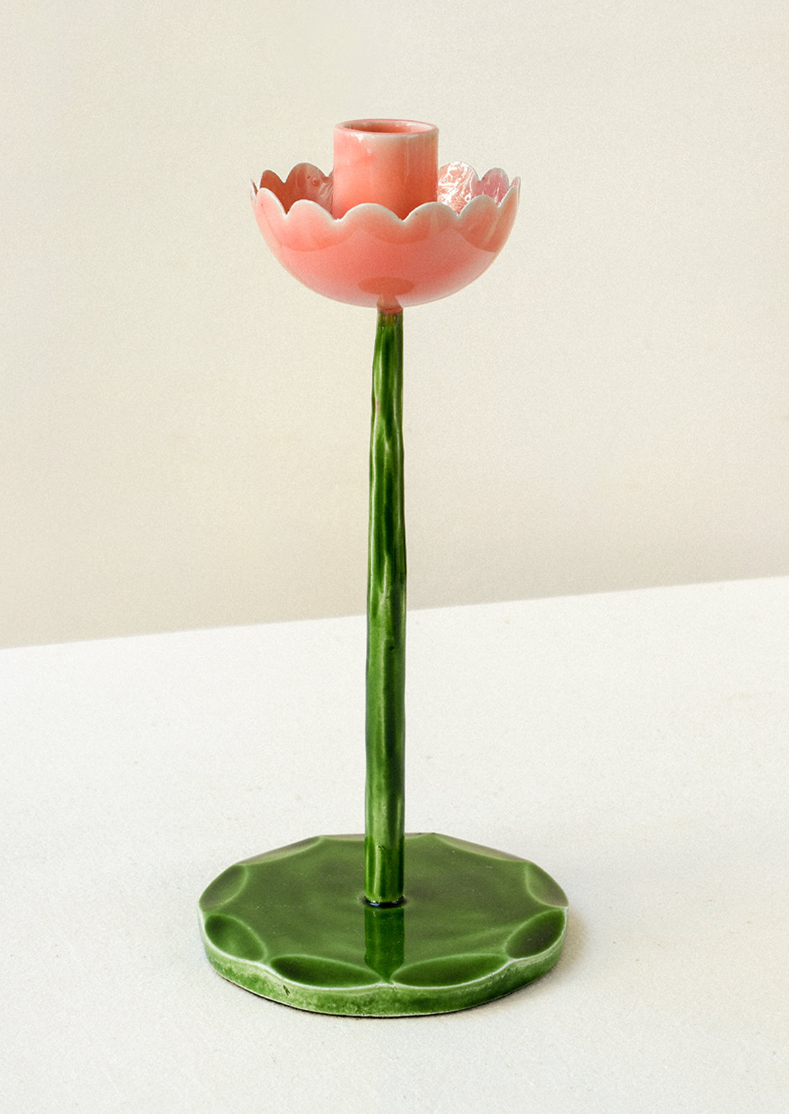 A taper holder in the shape of a flower with a pink top and green stem/base.