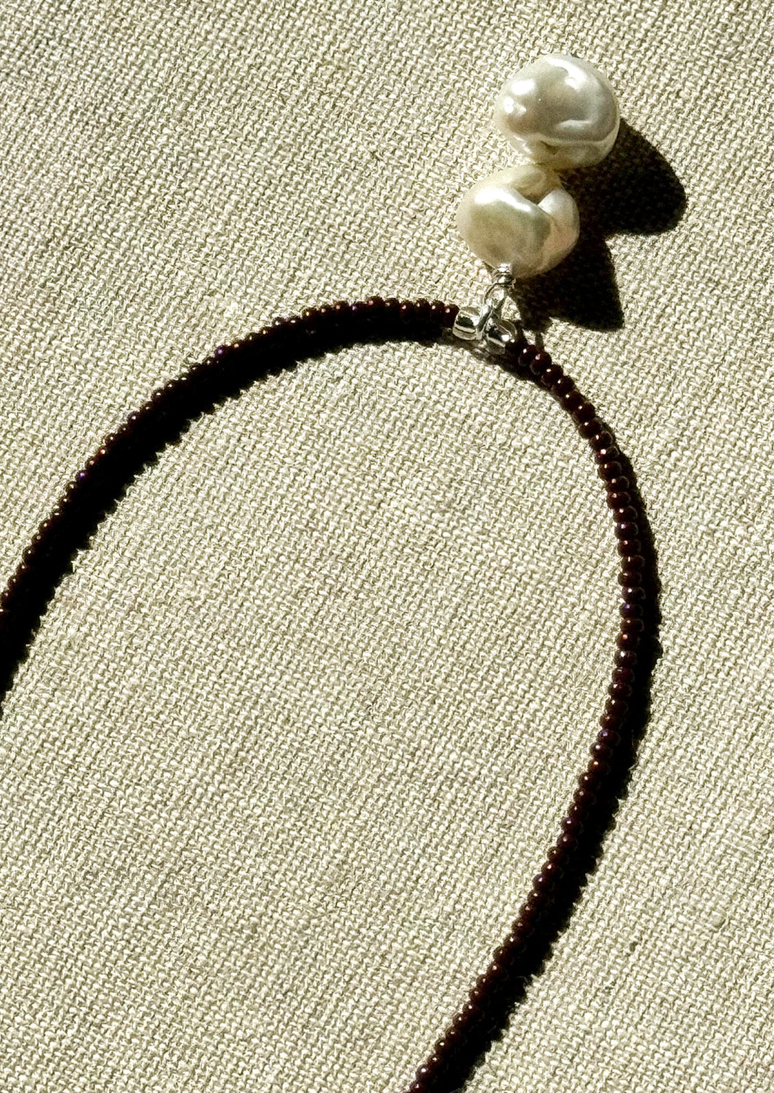 A necklace with small brown beads and a dangling freshwater pearl pendant.