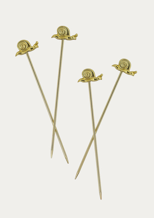 Four gold-toned cocktail picks with sculpted snail tops, arranged on a light gray background.