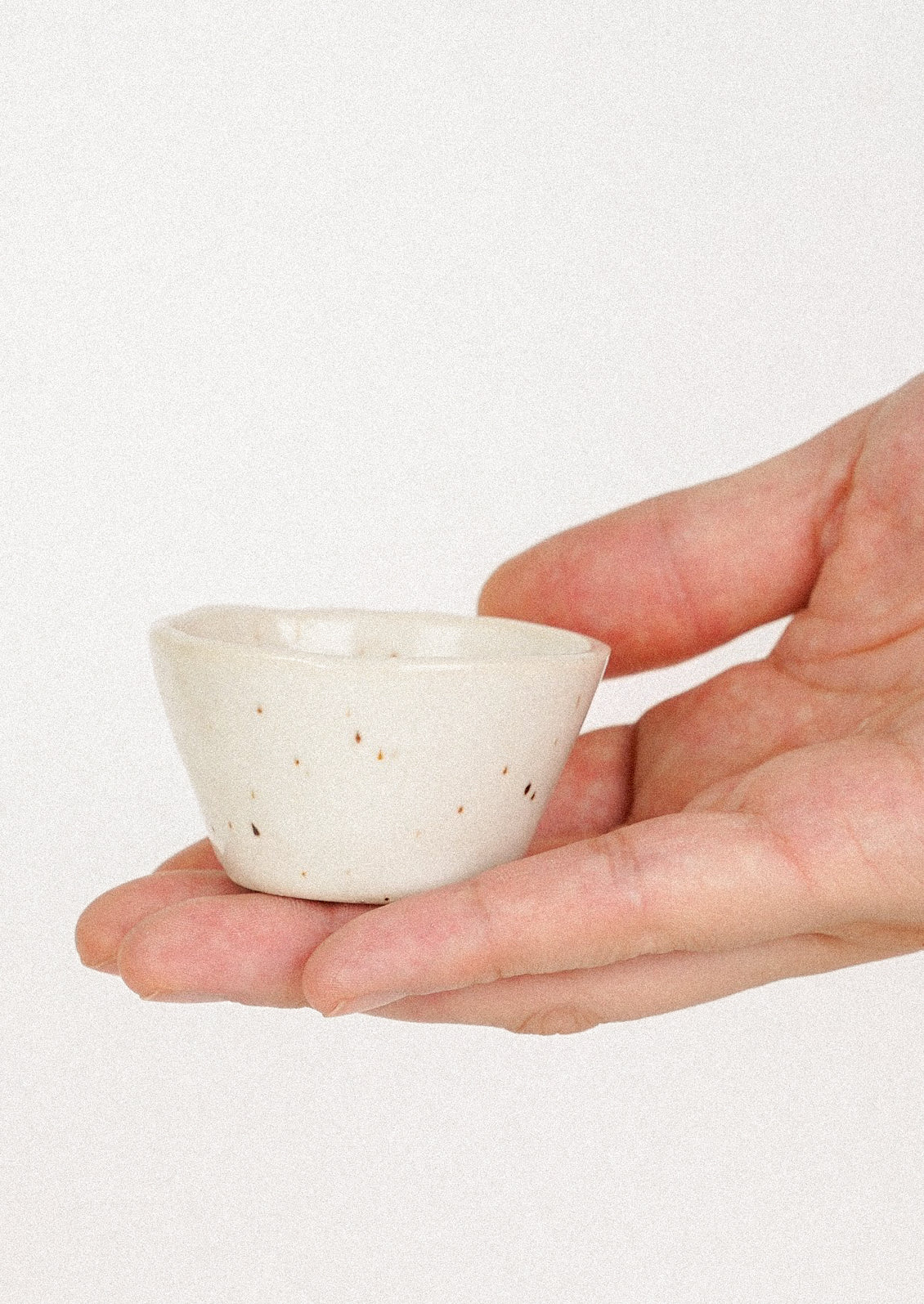 A hand holding a small ceramic bowl in cream.
